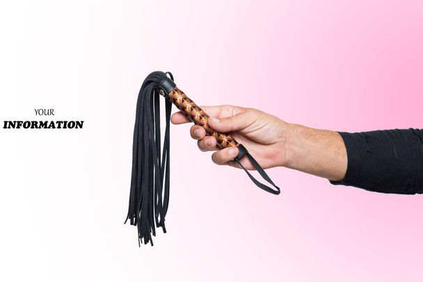 Leather whip in male hand good isolated on pink background in right side with space for text or logo. Strict black whip in man's hand. Accessories for adult sexual games. Toys for BDSM, flogging, sexual fetish and spanking devices - 写真・画像