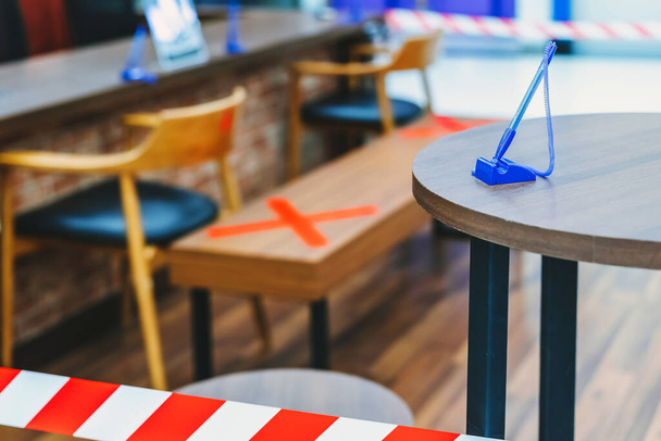 Un bolígrafo azul para transacciones en la mesa con imagen borrosa de marca de asiento alternativa para las reglas de distancia social en la distancia del centro comercial para un asiento de otras personas para proteger contra el virus Corona (COVID-19) - Foto, Imagen