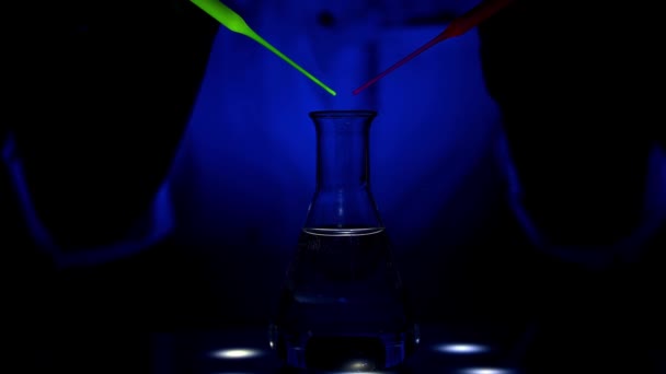 Een wetenschapper mengt een rode en groene kleur oplossing op een magnetische roerder UV-licht met de rollende beweging van het mengen in een chemisch laboratorium voor medische chemie - Video
