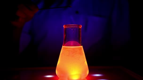 Naukowiec miesza rozwiązanie koloru czerwonego na mieszadle magnetycznym w niebieskim świetle z ruchem toczenia mieszania w laboratorium chemicznym do chemii medycznej - Materiał filmowy, wideo