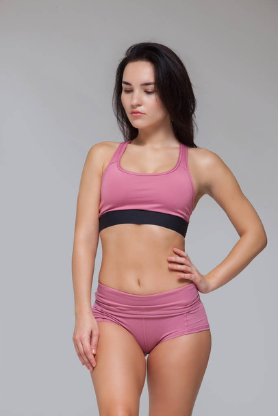 Attractive young brunette woman in pink sportswear is posing isolated on grey background - Foto, imagen