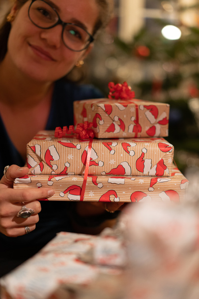 Hymyilevä tyttö antaa lahjoja ihanissa laatikoissa, joissa on lintujen muotoilu jouluaattona. Sumea tausta joulukuusen kanssa. - Valokuva, kuva