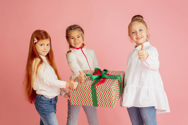 Noel tatilinde hediye vermek ve almak. Mutlu gülümseyen bir grup çocuk pembe stüdyo arka planında izole edilmiş eğleniyor. - Fotoğraf, Görsel