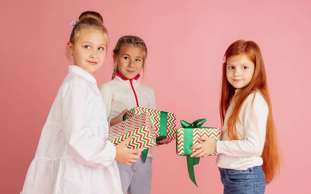 Giving and getting presents on Christmas holidays. Group of happy smiling children having fun isolated on pink studio background - Photo, Image