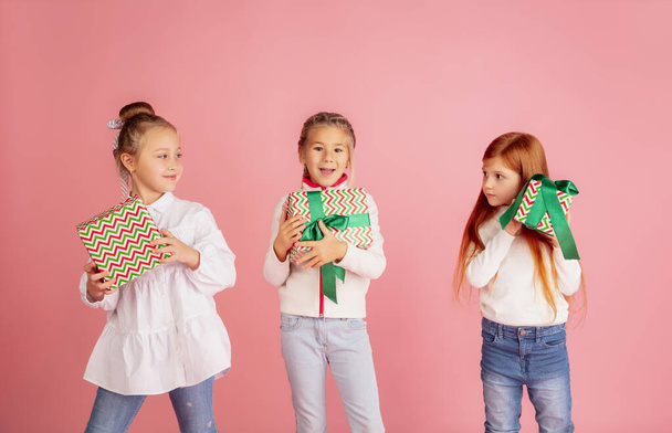 Giving and getting presents on Christmas holidays. Group of happy smiling children having fun isolated on pink studio background - Фото, изображение