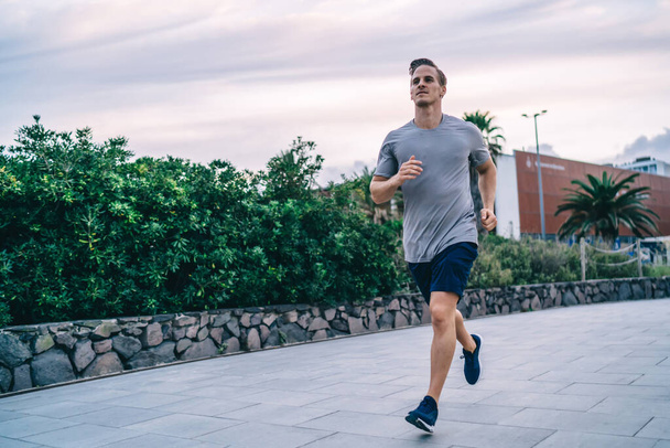 Handsome determined active male jogger enjoying energy and power during cardio training keeping healthy lifestyle,20s strong caucasian man with muscular strong body running on workout on city - Foto, Imagen
