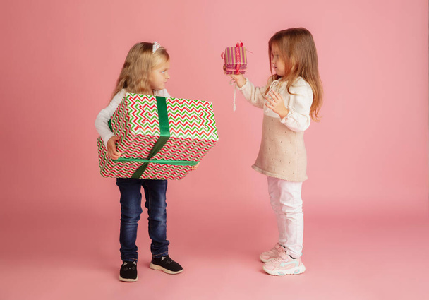 Giving and getting presents on Christmas holidays. Two little smiling children having fun isolated on pink studio background - Foto, Bild