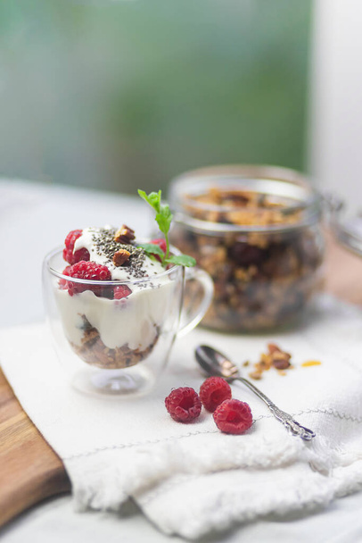 Granola in a jar and in a cup on a wooden board, served with yogurt and berries - Foto, Imagen