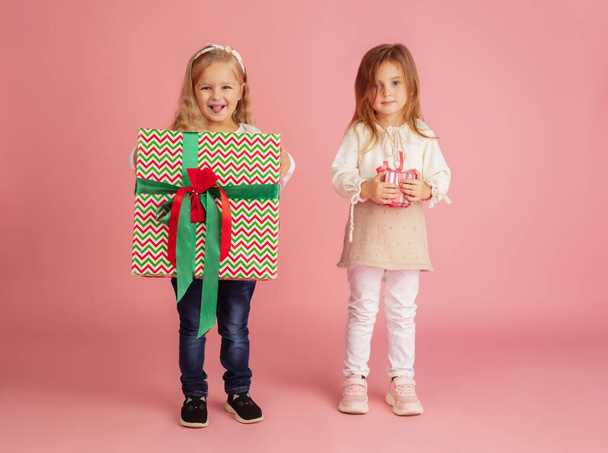 Giving and getting presents on Christmas holidays. Two little smiling children having fun isolated on pink studio background - 写真・画像