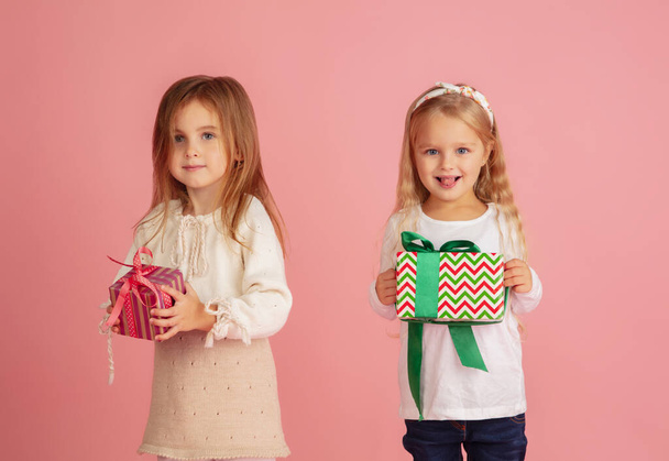 Schenken und Geschenke bekommen an Weihnachten. Zwei kleine lächelnde Kinder amüsieren sich isoliert auf rosa Studiohintergrund - Foto, Bild