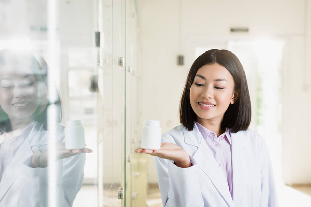 happy asian pharmacist in white coat pointing with hand in drugstore - Valokuva, kuva