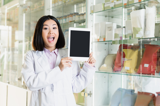innoissaan aasialainen farmaseutti valkoisessa takissa tilalla digitaalinen tabletti tyhjällä näytöllä apteekissa  - Valokuva, kuva