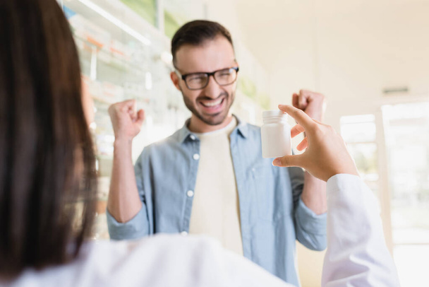 схвильований клієнт, дивлячись на фармацевта, який тримає пляшку з ліками на розмитому фоні
 - Фото, зображення