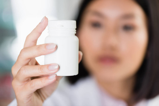 gyógyszeres üveg ázsiai gyógyszerész kezében homályos háttérrel - Fotó, kép