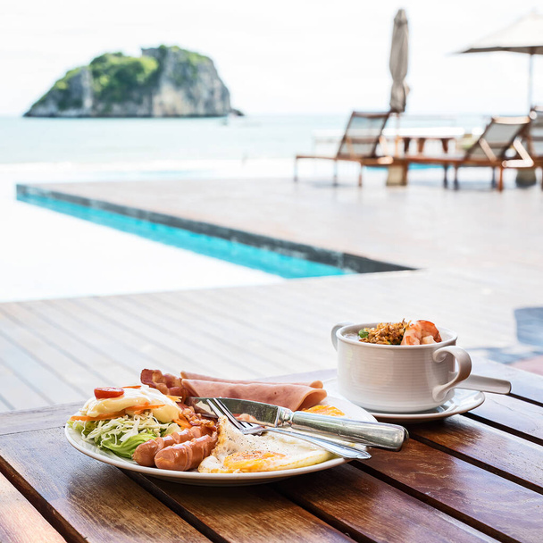 Английский завтрак состоит из жареных яиц, бекона, колбасы, и зеленый салат, и тайский рисовый суп с креветками с пляжным фоном в Таиланде - Фото, изображение