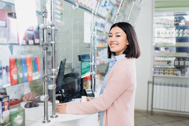 счастливый азиатский клиент держит бутылки с таблетками рядом с продавцом в аптеке  - Фото, изображение