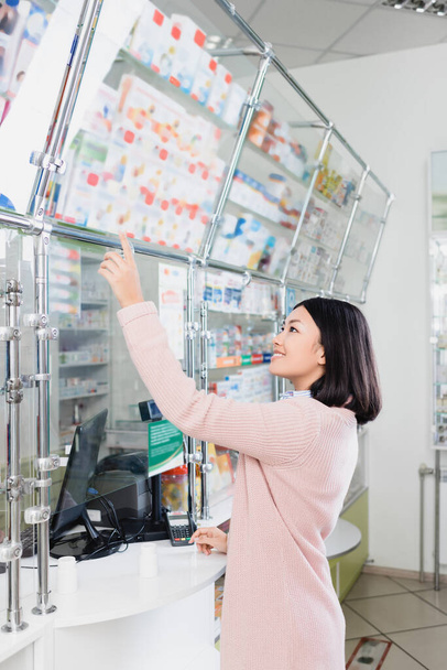 щасливий азіатський клієнт вказує пальцем на ліки в аптеці
  - Фото, зображення