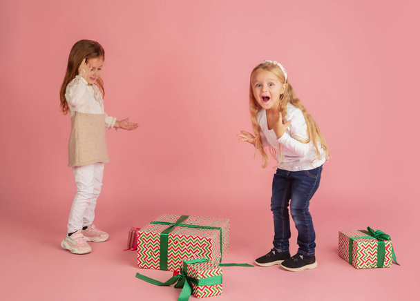 Giving and getting presents on Christmas holidays. Two little smiling children having fun isolated on pink studio background - Φωτογραφία, εικόνα