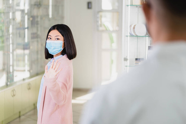 азіатська жінка в медичній масці махає рукою фармацевту в аптеці
 - Фото, зображення