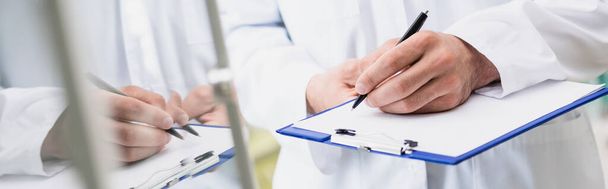 cropped view of pharmacist holding pen while writing on clipboard, banner - Fotoğraf, Görsel