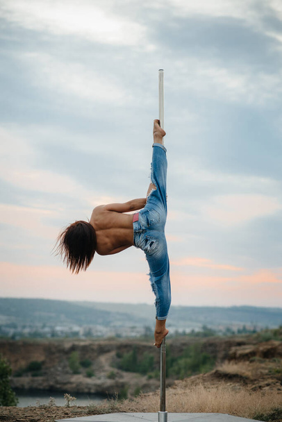A young sexy girl performs amazing exercises on a pole during a beautiful sunset. Dance. Sexuality - Fotografie, Obrázek