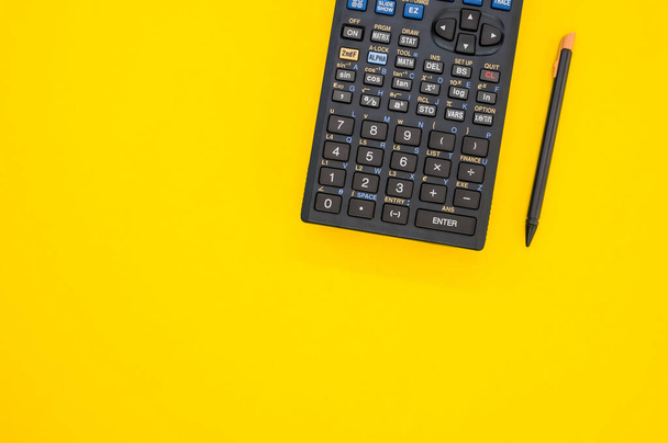 A closeup shot of a calculator and a pen on a yellow background - Foto, Bild