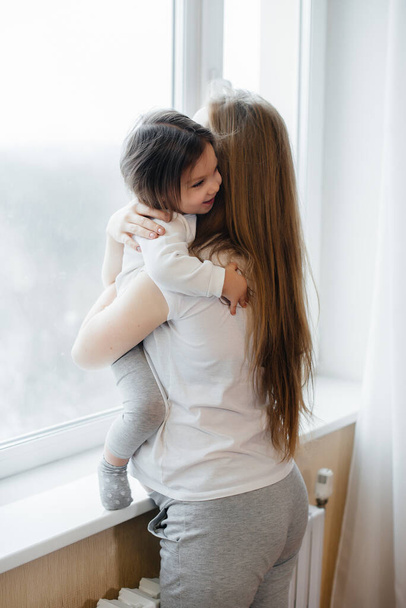 A pregnant mother is standing near the window with her little daughter - Zdjęcie, obraz