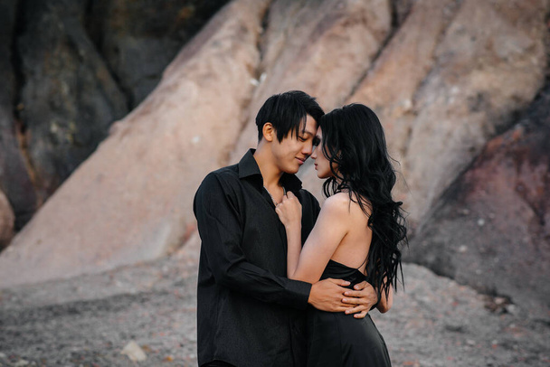 Una coppia asiatica innamorata in abiti di pelle nera passeggia nella natura tra gli alberi. Stile, moda, amore - Foto, immagini
