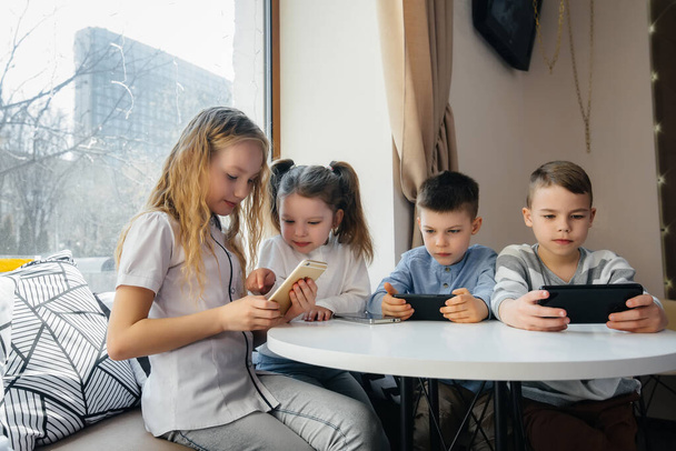 Children sit at a table in a cafe and play mobile phones together. Modern entertainment - Fotografie, Obrázek