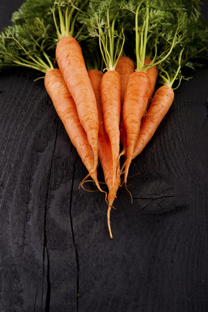 Букет свіжої моркви з зеленим листям на дерев'яному фоні
. - Фото, зображення