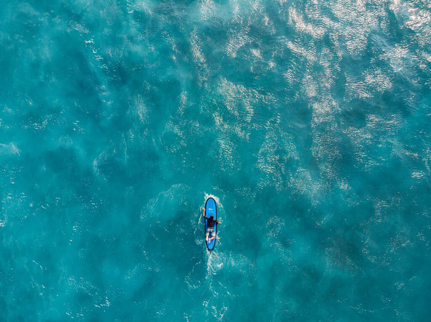 Aerial view of surfer on surfboard in blue ocean with foam. Top view - Zdjęcie, obraz