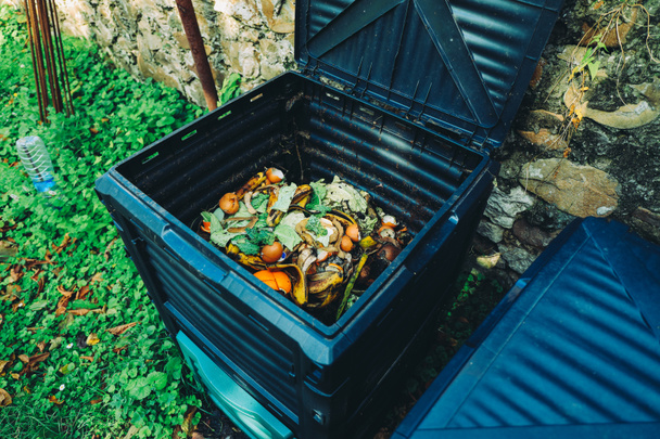 Compost bin with organic waste in the garden next to the stone wall. Organic farming and healthy lifestyle concept - Photo, Image
