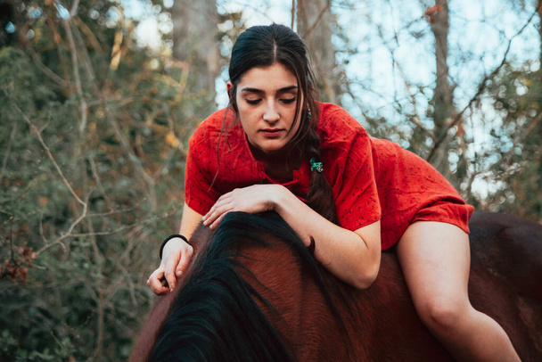 Bella giovane donna che abbraccia cavallo marrone e indossa vestito - Foto, immagini