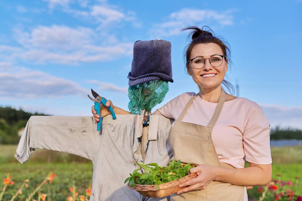 Donna contadina sorridente con cesto che abbraccia lo spaventapasseri nell'orto - Foto, immagini