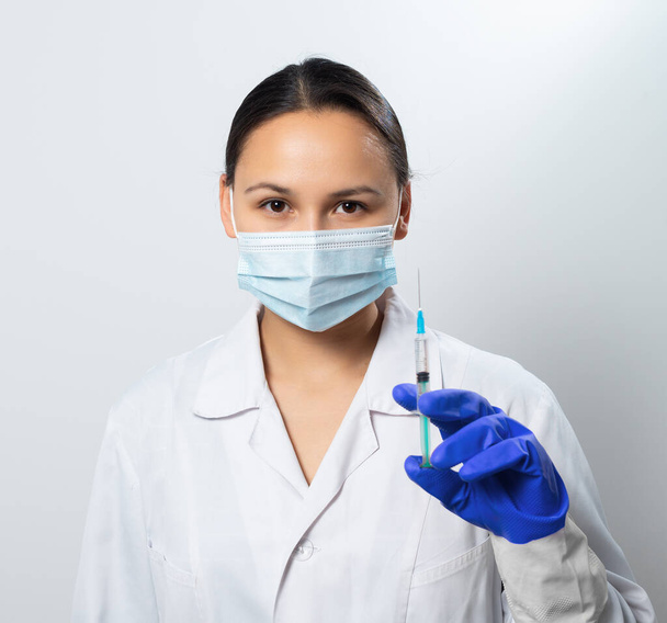 Woman doctor in a protective mask with a syringe in hand on white background. - Photo, image