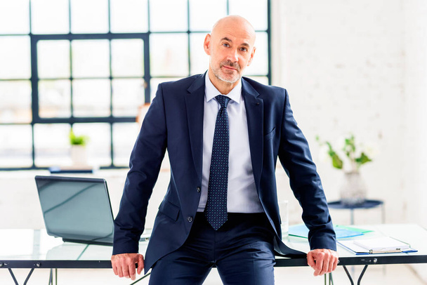Aufnahme eines lächelnden Geschäftsmannes in Anzug und Krawatte am Schreibtisch.  - Foto, Bild