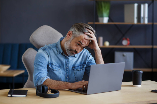 Tired and disappointed senior man working in home office with laptop. Portrait of handsome grey-haired manager sitting at workplace. Studying online, online courses. Burnout and overwork concept - Photo, image