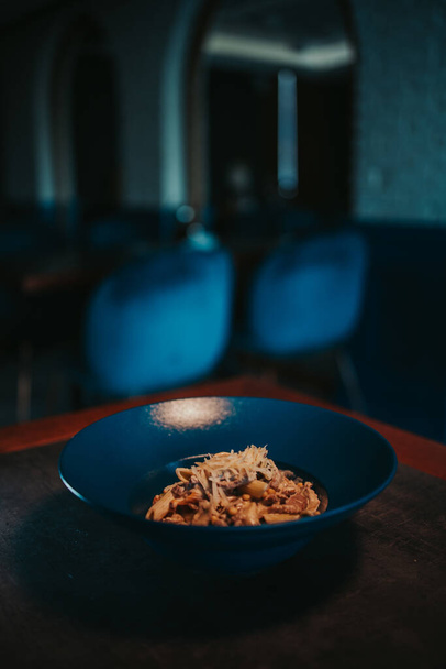 A vertical shot of a bowl of delicious penne pasta with meat, cheese, and sauce on the table - Foto, afbeelding