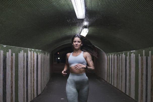 A young Europian woman with tattoos running in the tunnel during an outdoors workout - Fotografie, Obrázek