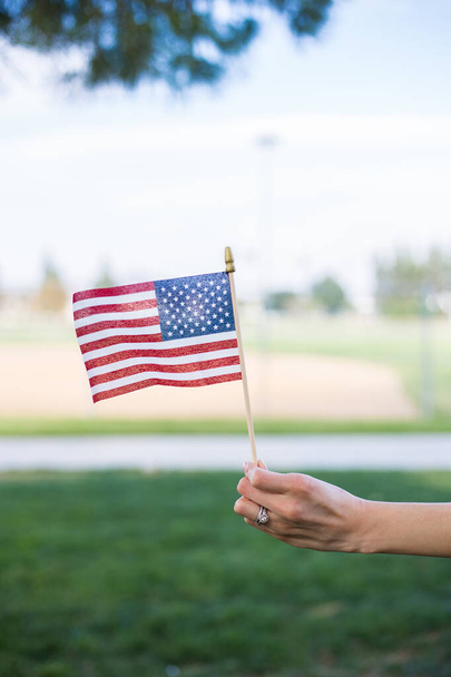 A vertical shot of a hand waving an American flag outdoors - Photo, image