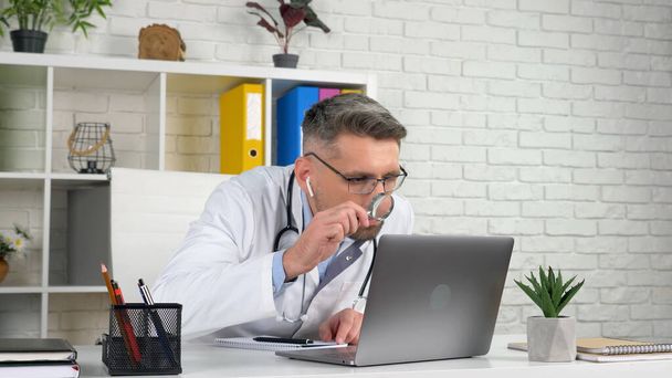 Доктор вивчає пацієнта онлайн відео виклик ноутбука веб-камера виглядає збільшуючи скло
 - Фото, зображення