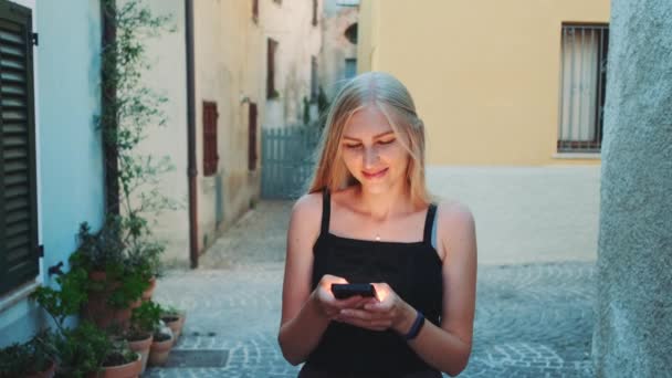 Kaunis nuori nainen juttelee älypuhelimella kävellessään kadulla - Materiaali, video