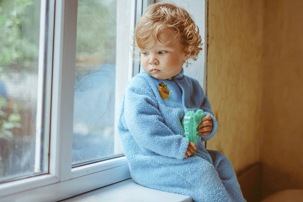 Küçük, ciddi bir çocuk pencerede oturuyor. - Fotoğraf, Görsel