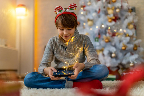Garçon utilisant un appareil mobile à la maison pendant la période de Noël - Photo, image