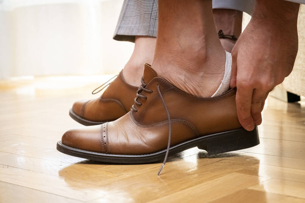 A closeup of the bridegroom wearing his elegant and luxury brown shoes for the wedding - Fotó, kép
