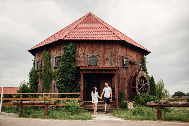 Couple in love walks near a large wooden mill on summer day. man and woman are having fun outdoors - Фото, изображение