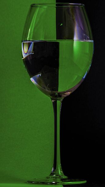 A vertical shot of a glass of water on a green and black background - Fotoğraf, Görsel