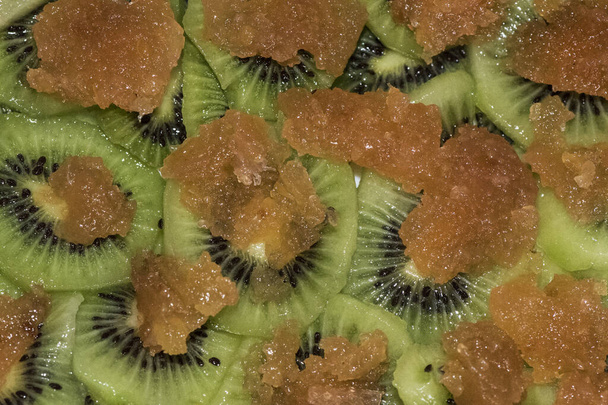 Seizoensgebonden kiwi-schijfjes in het groen met hun roggen en zaden, vergezeld van verduurzaamd kweepeer licht door flits - Foto, afbeelding