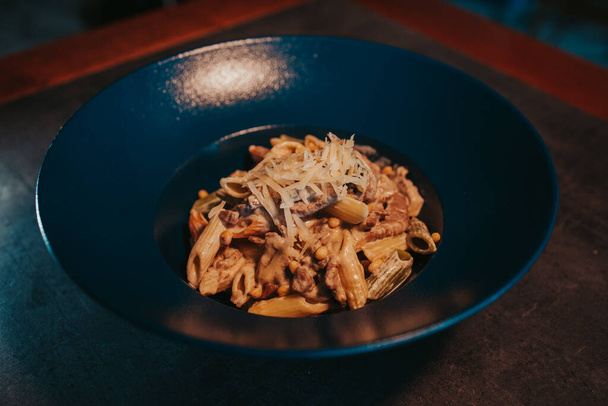 A closeup of delicious penne pasta with meat, sauce, and grated cheese in a bowl on the table - Fotó, kép