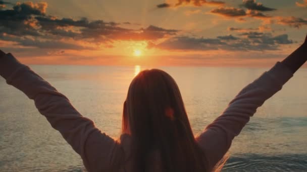 Giovane donna con le braccia tese godendo la bellezza del tramonto sul mare - Filmati, video